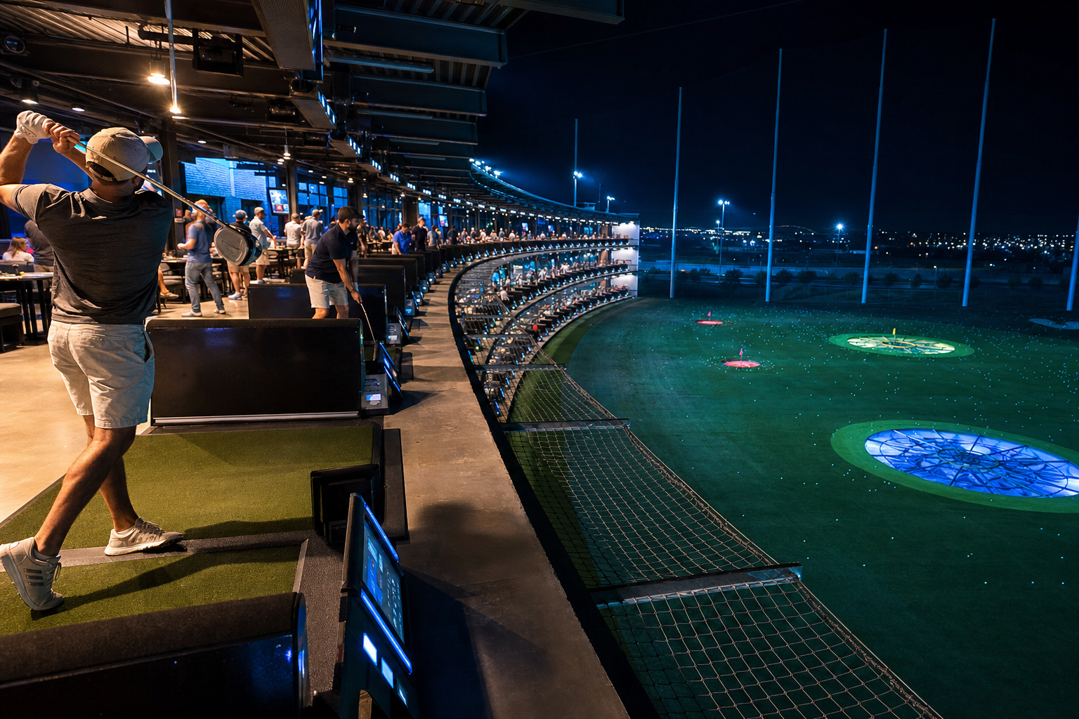 Floodlit driving range at dusk — illustrative; a real photo would show lit Toptracer bays with players hitting onto a green target field